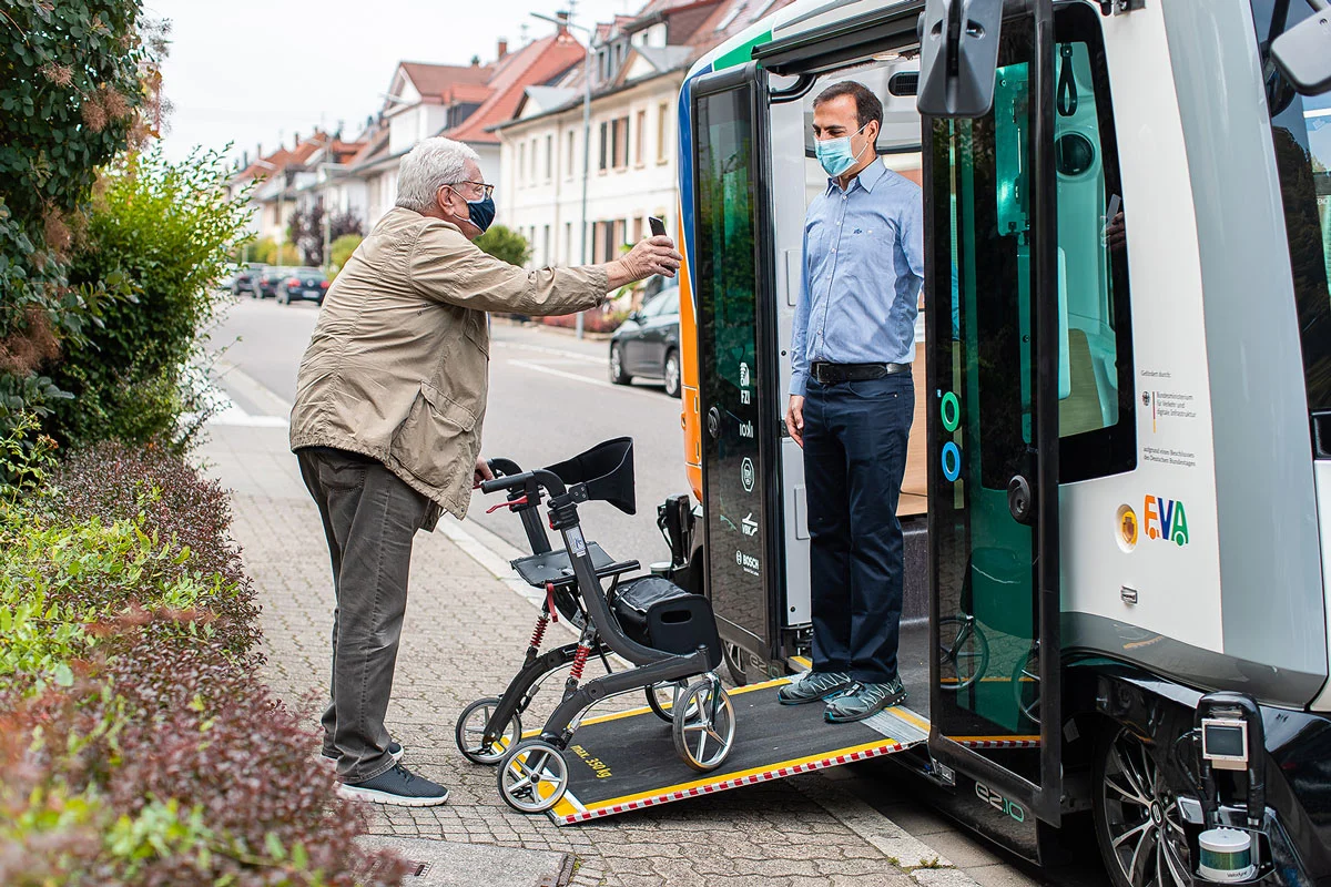 Ein älterer Mann mit Rollator scannt ein Ticket an einem autonom fahrenden Shuttlebus.