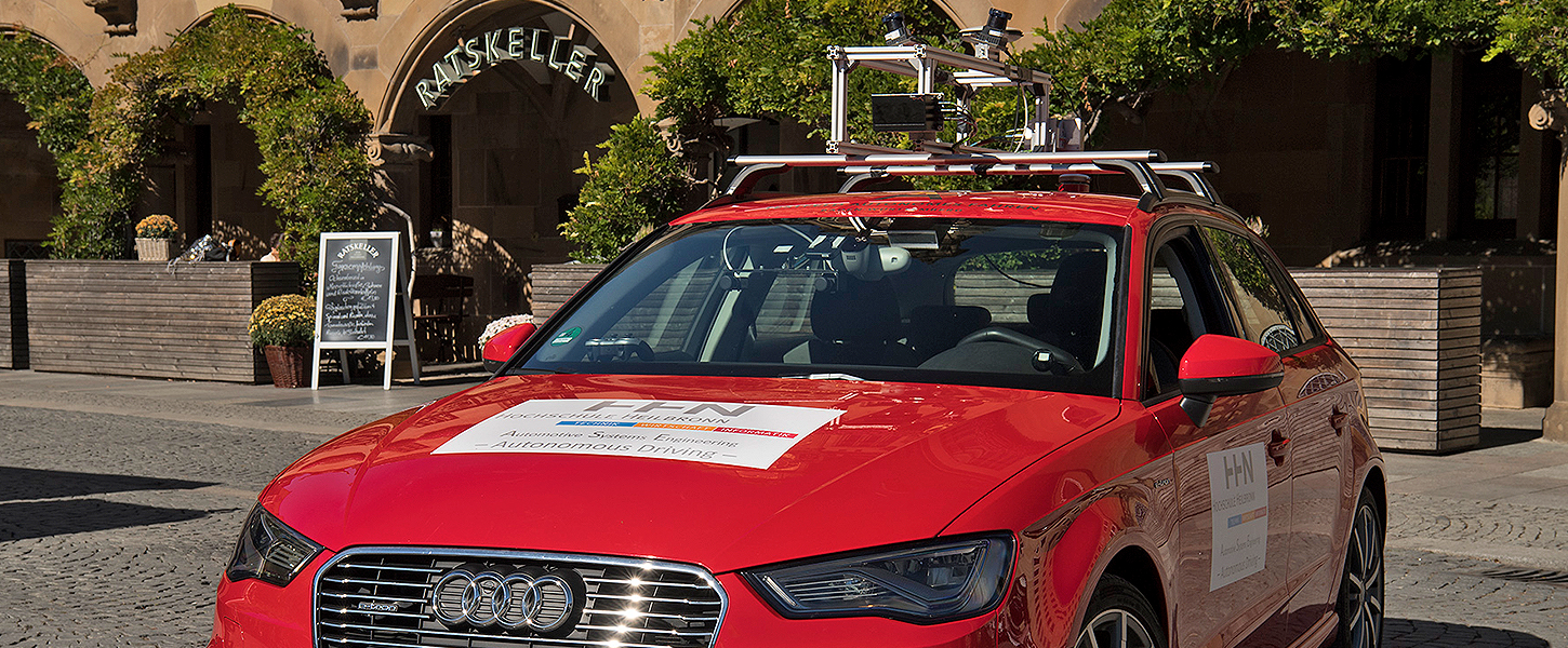 Ein roter Audi mit umfangreicher Messtechnik auf dem Dach, beschriftet mit „Autonomous Driving“.